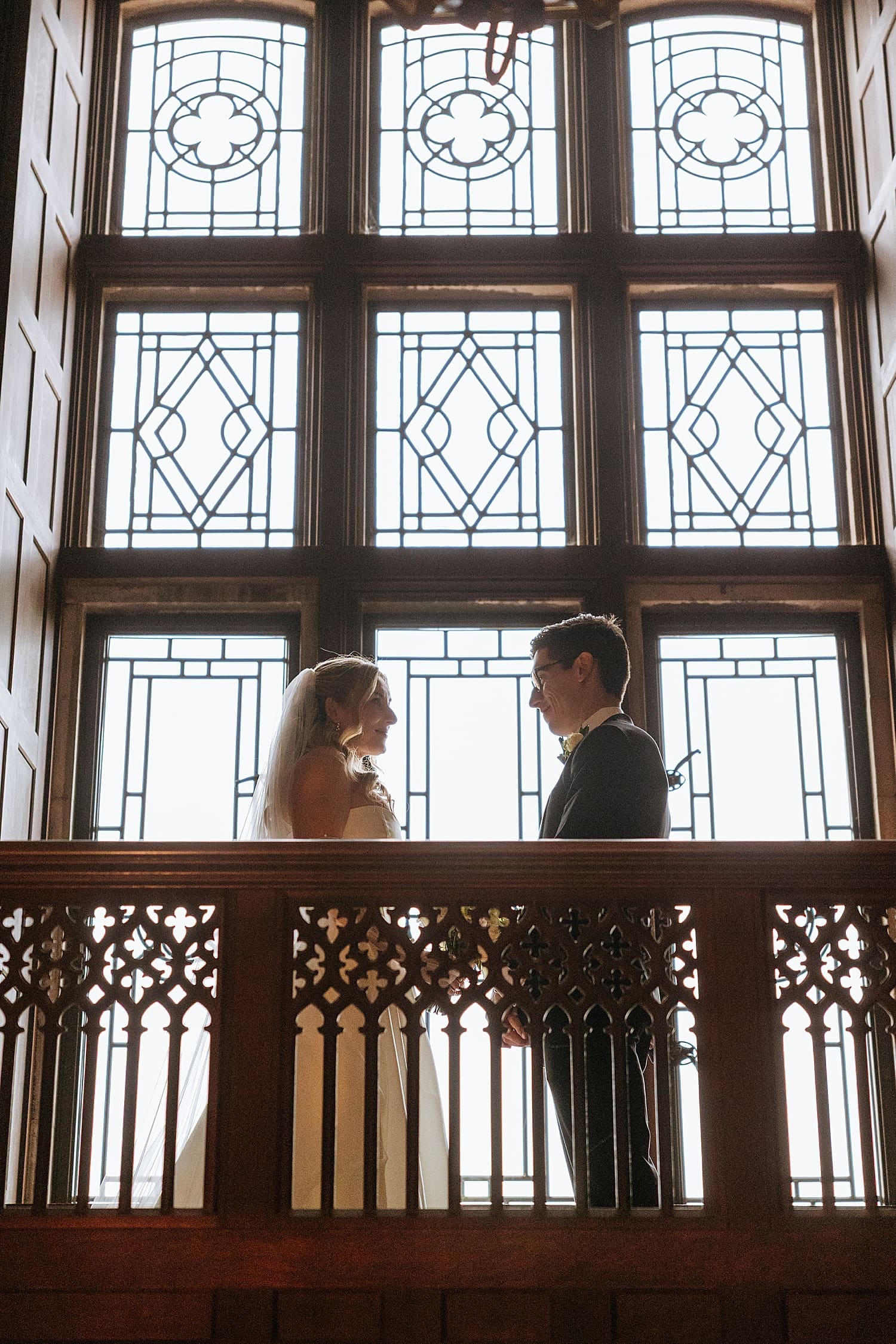 couple stands on indoor balcony in front of historic windows by East Coast wedding photographer