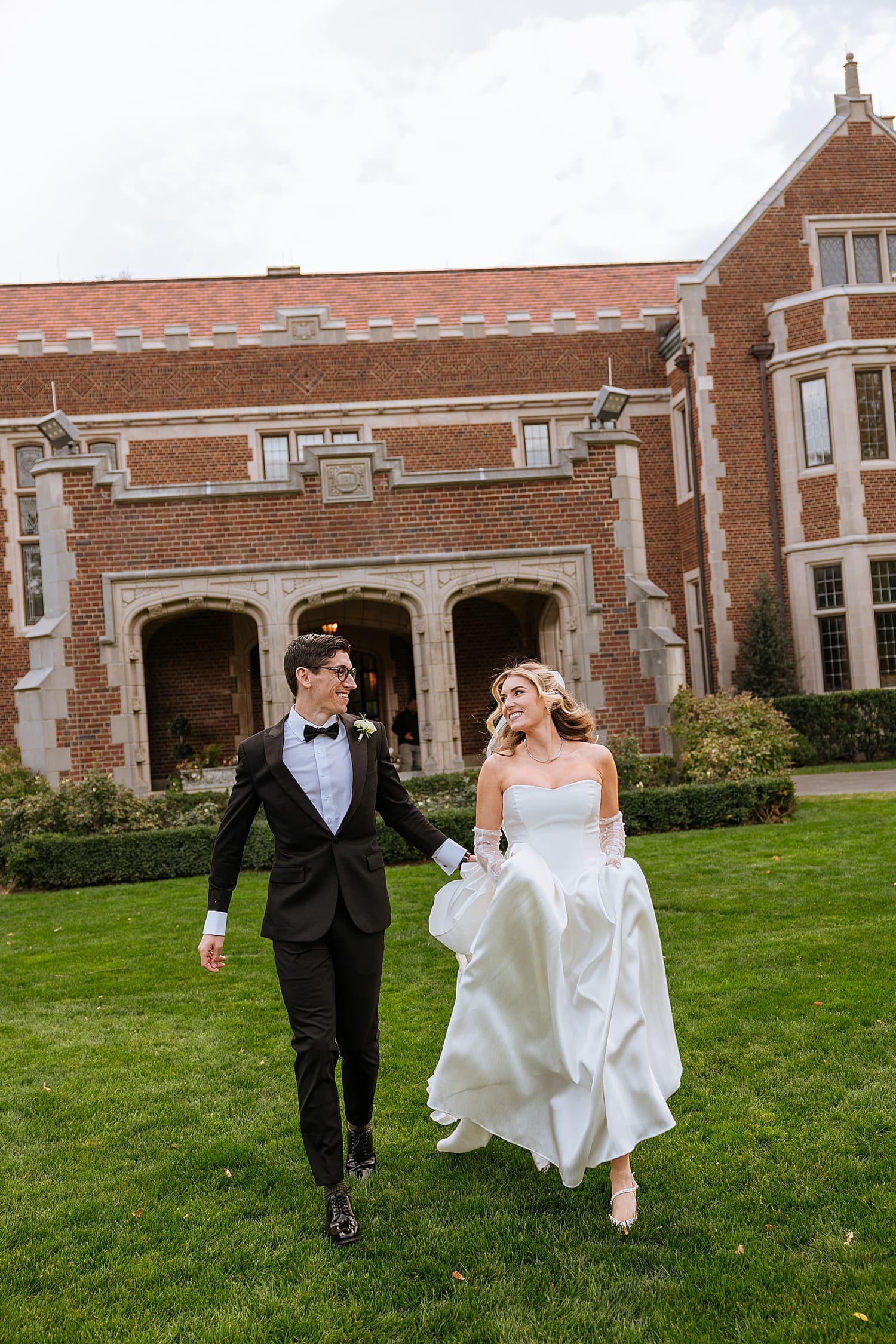 newlyweds run down a lawn in front of old estate by East Coast wedding photographer