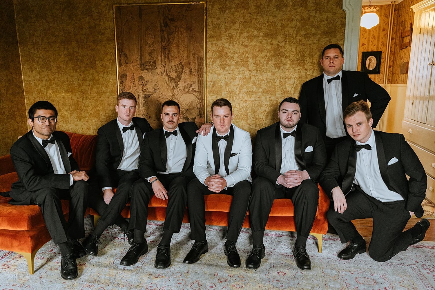 groomsmen sit in front of gold wall by East Coast Wedding Photographer