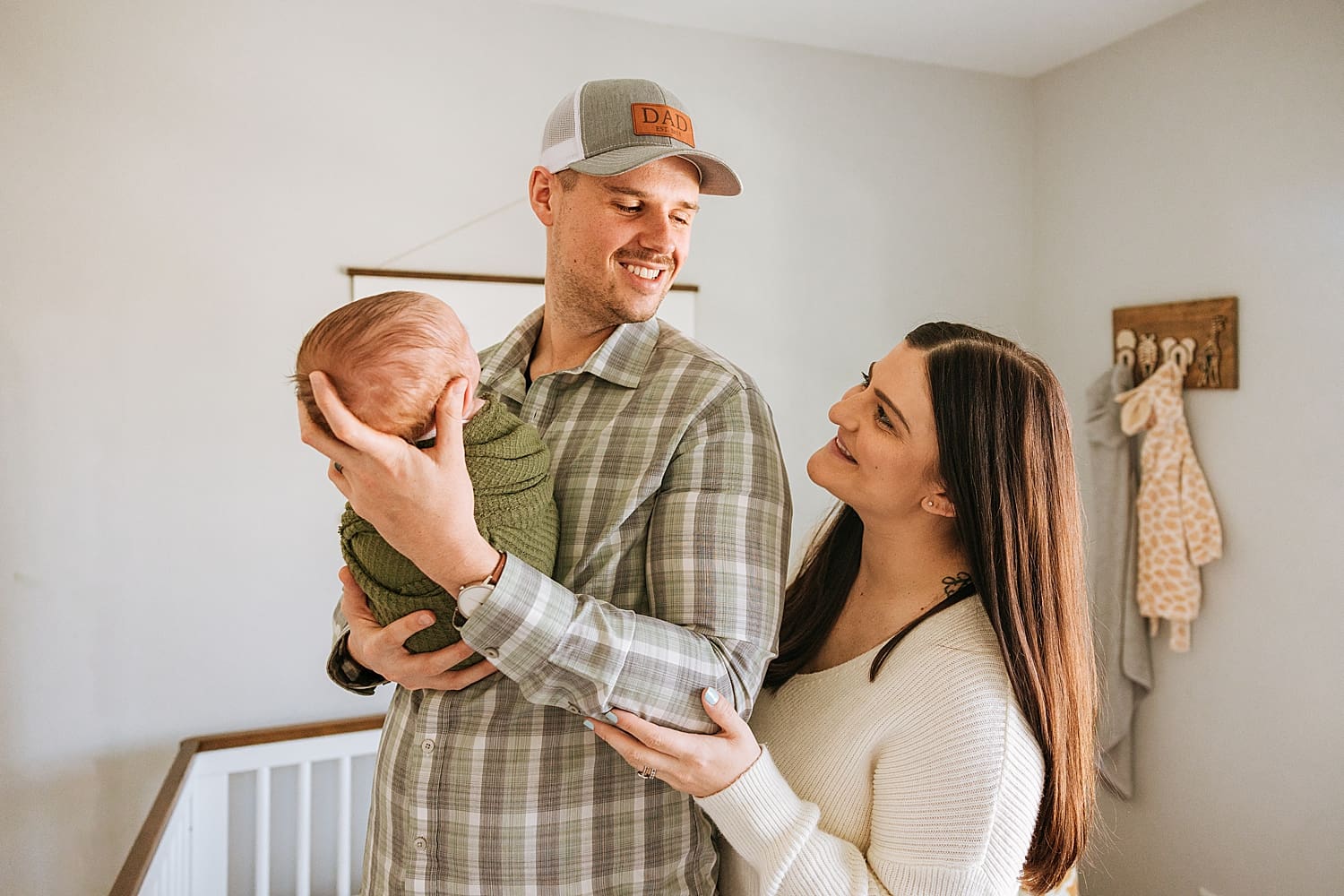new parents smile at each other while holding baby in nursery by Kelly Jean Photography